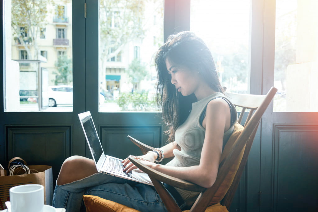 Asian girl working at a coffee shop with a laptop.female freelancer connecting to internet via computer.flare light